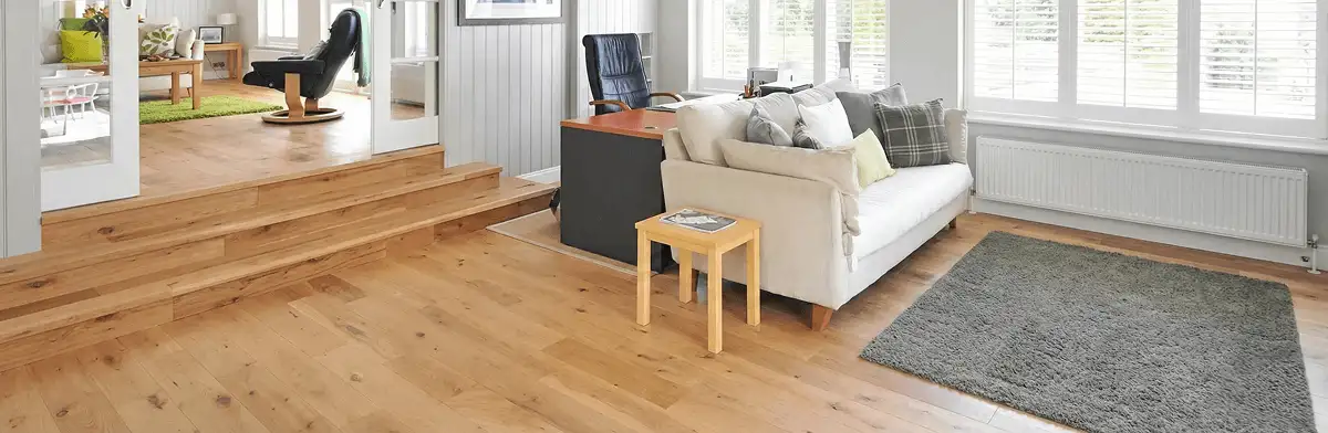 A modern living room with professionally installed laminate flooring, a beige sofa, a small side table, a gray rug, and large windows with white shutters in Charlotte, NC